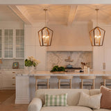 A transitional kitchen with two Talin Lantern Pendants in chestnut and matte brass hanging over a white marble island under a coffered beamed ceiling.