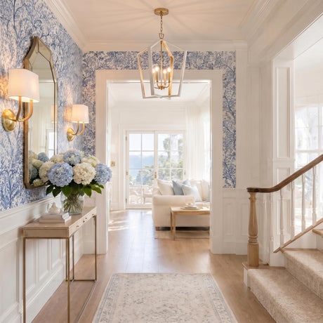 A transitional foyer with a white and matte brass Talin Lantern Pendant 20" over light wood flooring, blue botanical wallpaper, and a slim console table.