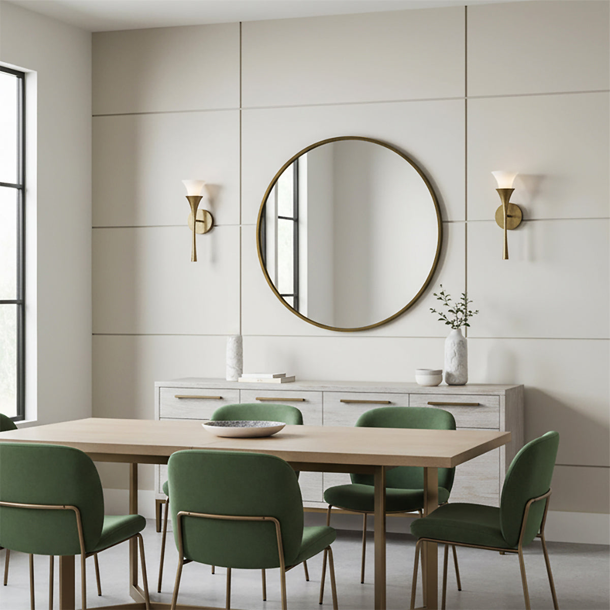 Fleur Wall Sconce 16, Textured Brushed Brass - Two brass wall sconces with white glass shades flank a round gold mirror above a sideboard in a dining room with green chairs around a wooden table.