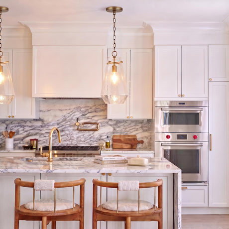 A transitional kitchen featuring the Delmar Pendant 11", Aged Brass hanging over a marble waterfall island with white cabinetry and a matching marble backsplash.