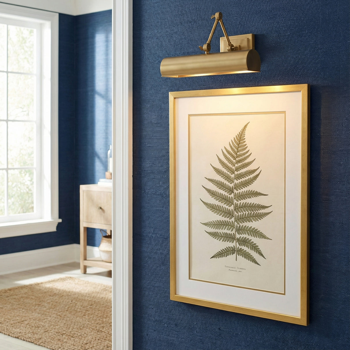 Henry Picture Light 16", Aged Brass linear picture light in a Transitional Entryway with a gold fern print and navy textured wall.