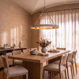 A coastal dining room with the Saltair Ring Chandelier in matte brass and natural rope over a light wood table under a sloped ceiling with textured walls.