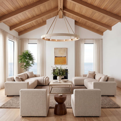 A coastal living room with the Saltair Ring Chandelier in matte brass and natural rope hanging from a vaulted wood ceiling above beige sectional sofas.