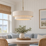 A coastal dining nook with a two-tiered natural rope pendant in brass suspended above a round wood dining table with blue banquette seating.