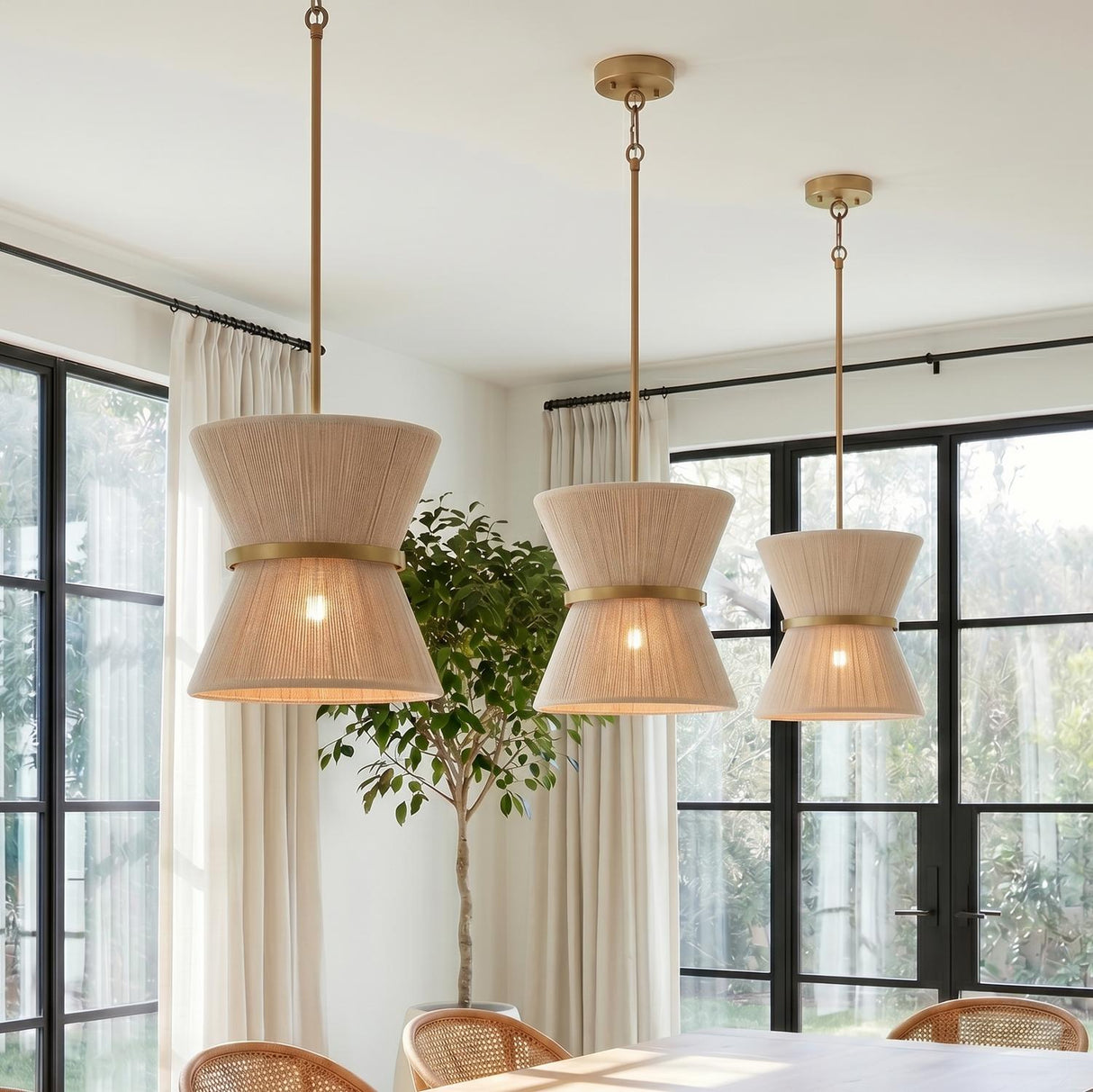A transitional dining room with three Beacon Pendants in patina brass and natural rope hanging over a wooden table near large black steel windows.
