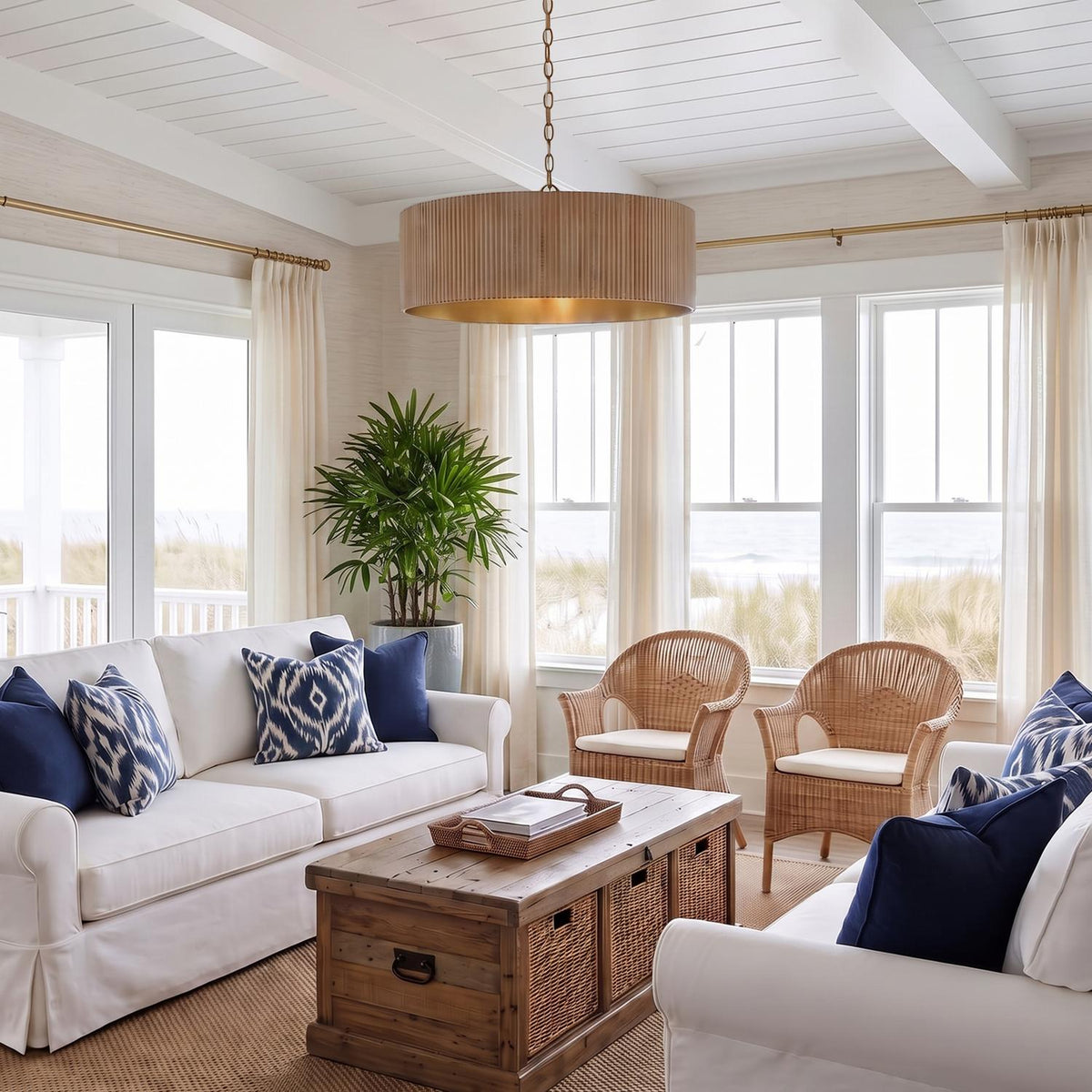A coastal living room with the Leery Pendant 31-inch, Whitewash and Matte Brass over a wood trunk coffee table under a white beamed ceiling.