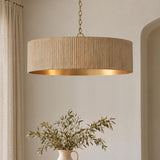 A transitional dining room features a whitewash ribbed drum pendant with a brass interior hanging over a ceramic vase with olive branches and linen drapes.