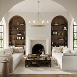 living room with white sofas, wooden arched book shelves and the Maren 6 Light Chandelier 31", in Whitewash and Matte Brass on and glowing.