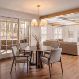A transitional dining room with the Simone 4 Light Chandelier 27", Matte Brass over a round walnut table and grey upholstered chairs near large glass doors.