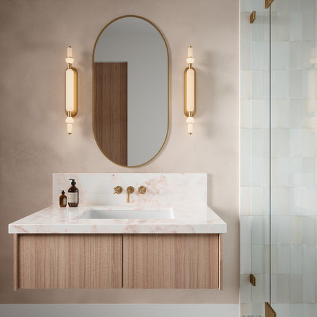 Two Giselle 31" LED vanity lights in brass shown with a bathroom vanity with marble countertop, wooden cabinet, and oval mirror.