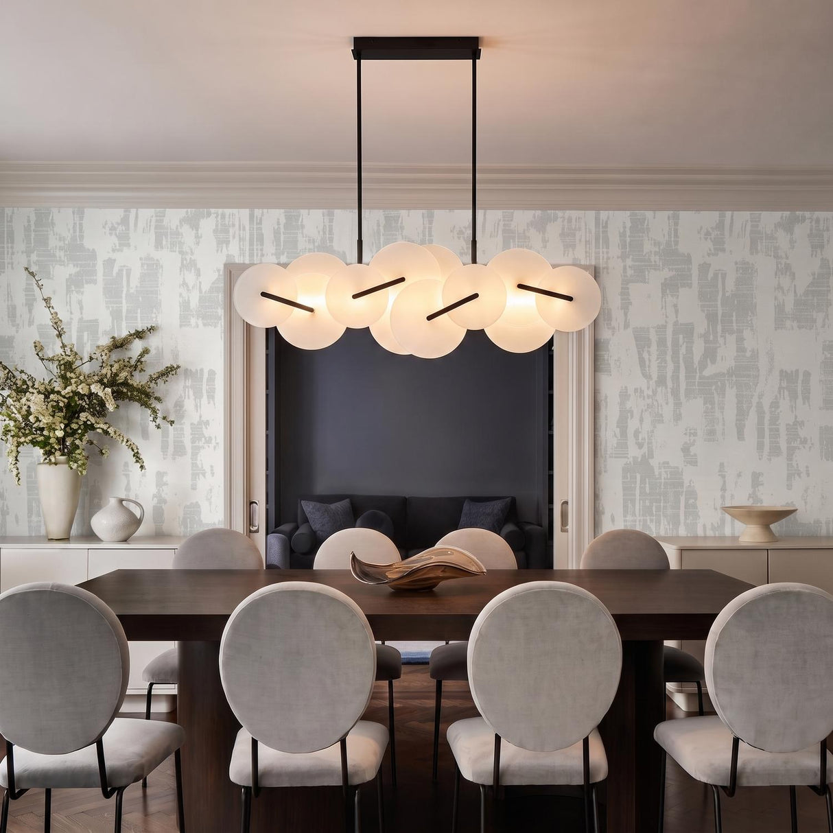 A contemporary dining room with the Malya LED Linear Chandelier in matte black and opal glass over a dark wood table with gray velvet chairs.