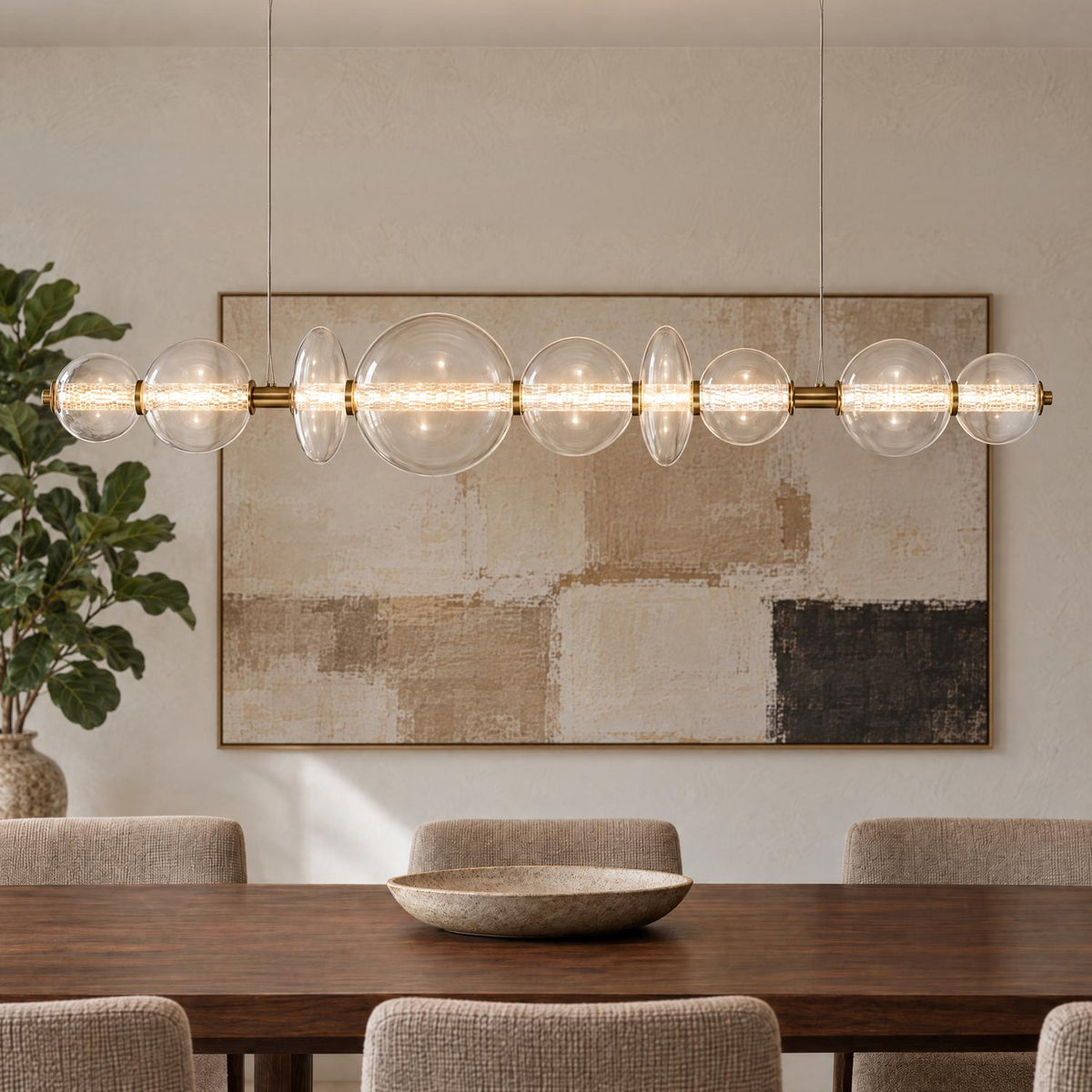 A modern dining room with the Elara LED 9 Light Linear Chandelier 74", Brass and Clear Glass suspended over a dark wood table and neutral artwork.