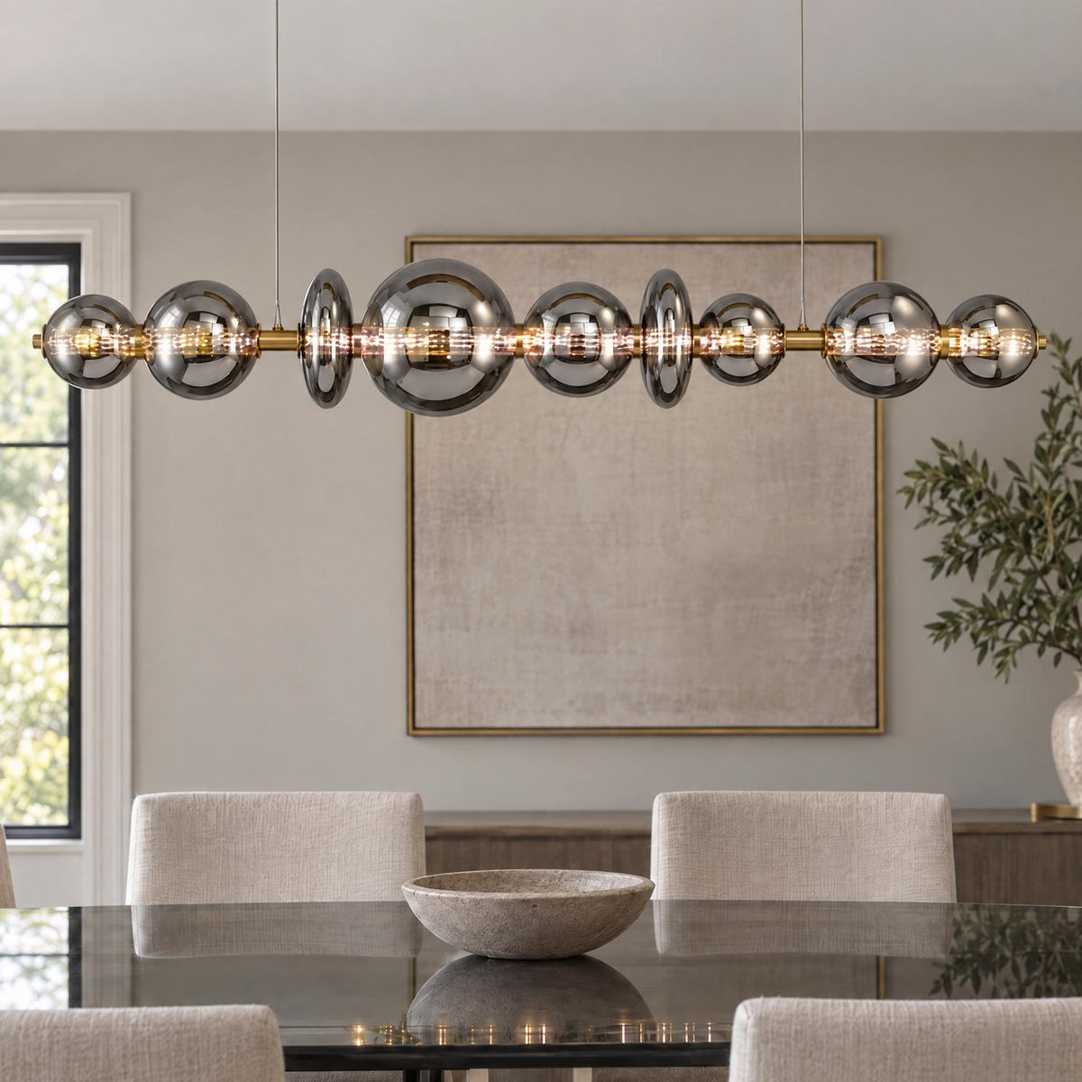 A contemporary dining room features the Elara LED 9 Light Linear Chandelier 74", Brass and Smoke Glass above a dark reflective table and neutral upholstered chairs.