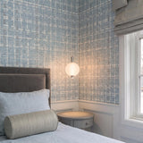 A contemporary bedroom with a Nola LED Pendant in polished nickel and ribbed opal glass hanging over a gray nightstand against blue textured wallpaper.