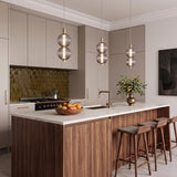 A contemporary kitchen featuring three brass and ribbed smoked glass pendants over a white marble island and walnut cabinetry with an olive green tile backsplash.