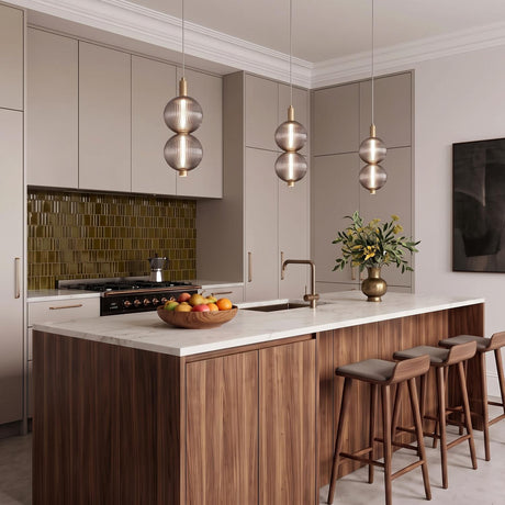 A contemporary kitchen featuring three brass and ribbed smoked glass pendants over a white marble island and walnut cabinetry with an olive green tile backsplash.
