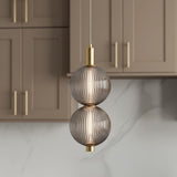 A contemporary kitchen features the Nola LED 2 Light Pendant 6", Brass and Ribbed Smoked Glass suspended over the island against taupe shaker cabinets and marble backsplash.