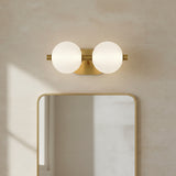 Nola LED 2 Light Vanity 15, Brass and Ribbed Opal Glass - A brass vanity light with two ribbed opal glass globes mounted above a gold-framed mirror against a textured cream wall.