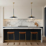 A contemporary kitchen features two Yates LED Pendant 30", Matte Navy with brushed brass accents over a marble waterfall island and navy cabinets with leather stools.