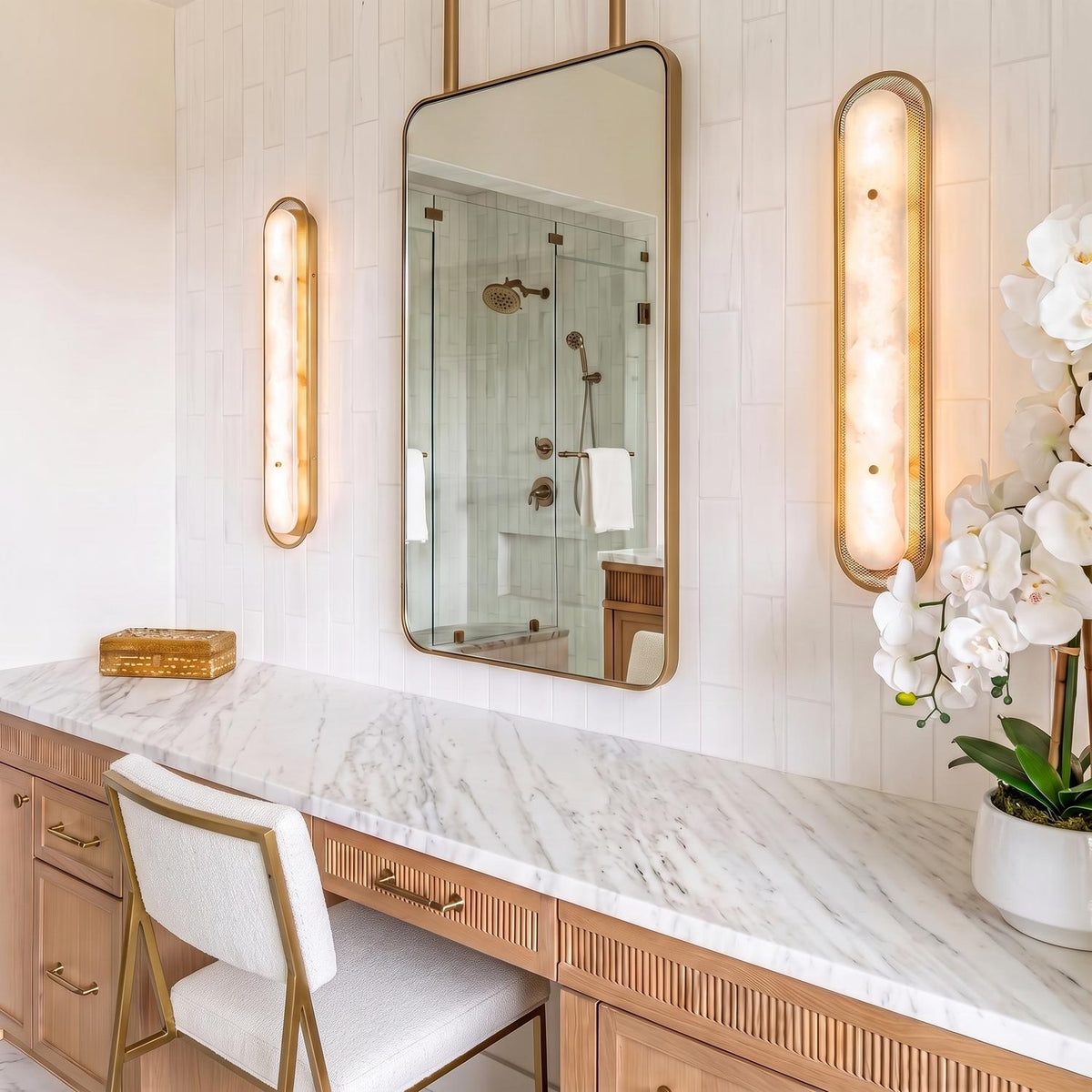 A transitional bathroom features the Vance LED Wall Sconce 38", Brass and Alabaster flanking a framed mirror over a white marble vanity with fluted drawers.