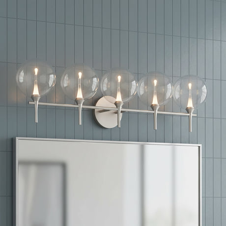 Eaton LED 5 Light Vanity, Satin Nickel and Clear Glass - A five-light vanity fixture with clear globe shades and satin nickel accents mounted above a mirror against a grey tiled wall.