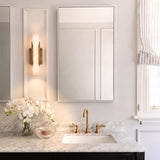 A transitional bathroom featuring the Delya LED wall sconce in antique brass and alabaster mounted on a white paneled wall beside a marble vanity and brass faucet.