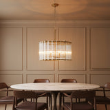 Nori 6 Light Chandelier 24, Brass and Ribbed Glass - A brass chandelier with ribbed glass hangs over a dining table with brown chairs.