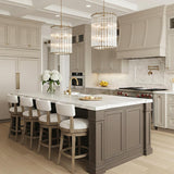 A transitional kitchen features two Nori 8 Light Chandelier 22", Brass and Ribbed Glass fixtures in brushed brass over a white marble island under a coffered ceiling.