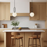 A modern kitchen featuring two Oren Pendant 10", Matte Black and Opal Glass fixtures over the island, accented by light wood cabinets and a marble backsplash.