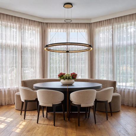 A contemporary dining room featuring the Lune LED Pendant 48", Brass and Black over a dark round dining table with beige chairs and sheer drapes.