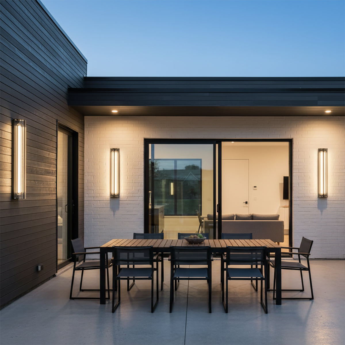 Prescott LED Outdoor Wall Light 24 - Two modern outdoor wall lights illuminate a patio area with a dining table and chairs.