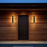Rye LED Outdoor Wall Light 21, Textured Black - Two black sconces illuminate a black door on a wood paneled wall.