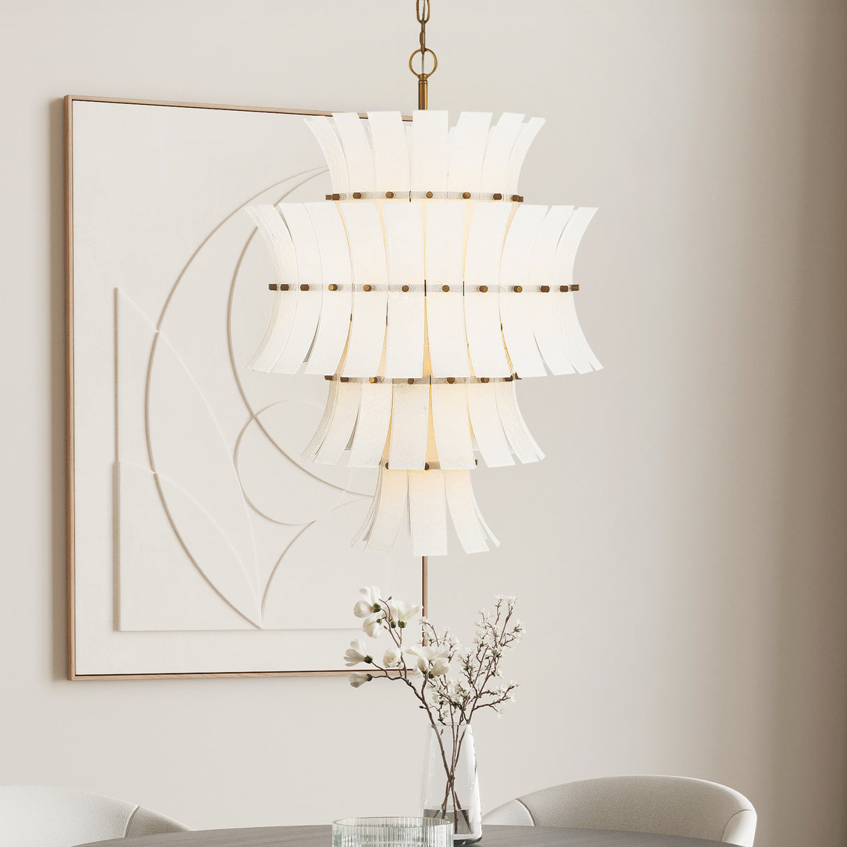 Brielle 13 Light Chandelier finished in  White Art Glass with Aged Brass is shown in a bright dining area in front of modern art. 