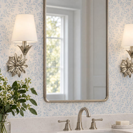 A traditional bathroom features the Ayla Wall Sconce 15", Antique Silver with white fabric shades flanking a mirror against blue floral wallpaper above a marble vanity.