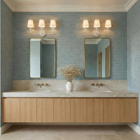 A coastal bathroom with blue grasscloth wallpaper featuring two Ayla 3 Light Vanity, Matte White fixtures with linen shades mounted above gold framed mirrors.