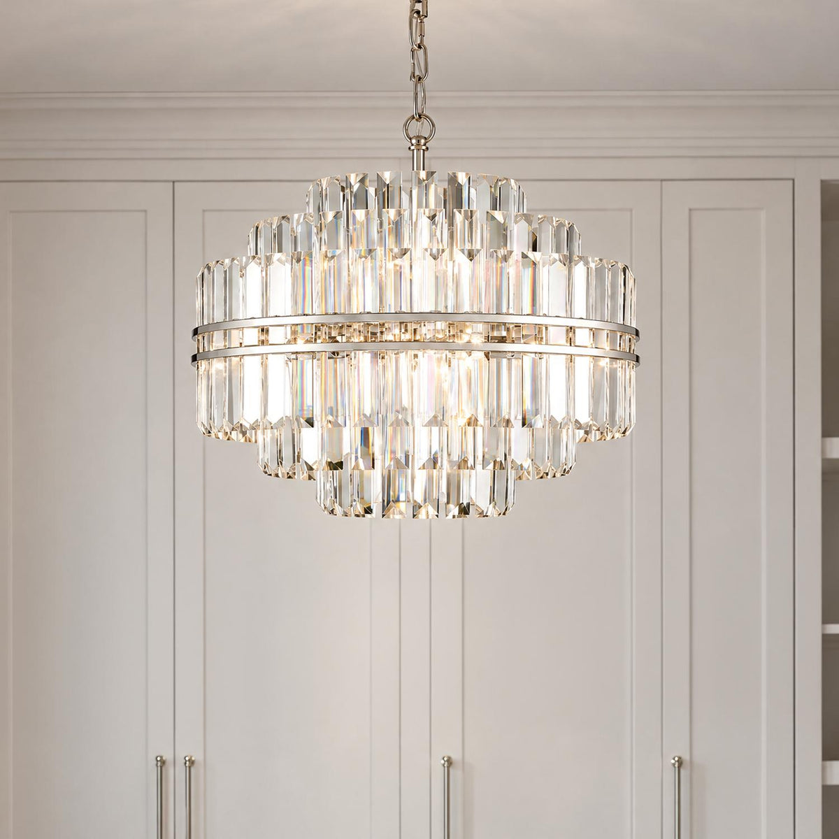 A transitional closet featuring the Maxwell 12 Light Chandelier 22", Crystal with Polished Nickel suspended in front of off-white paneled wardrobe cabinets.