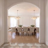 A transitional dining room featuring two Maxwell 16 Light Chandelier 28-inch crystal and polished nickel fixtures hanging over a wood table viewed through a white arched entryway.