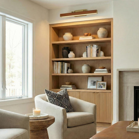Jarrett LED Picture Light 32", Aged Brass and Cognac Leather linear Wall Sconce in a Transitional Living Room with oak bookshelves.