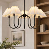 A transitional living room displays the Rory 5 Light Chandelier 31", Matte Black with pleated fabric shades beside light wood built-in bookshelves and framed artwork.