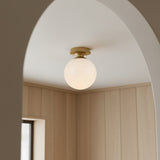 Amos Semi-Flush 8", Brushed Brass with Milk Glass ceiling light in a room with wooden paneling and an archway.