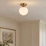 A transitional foyer featuring the Amos Semi-Flush 8", Brushed Brass with Milk Glass mounted on a ceiling near cream paneled cabinetry and framed botanical art.