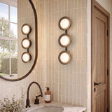 A modern bathroom featuring the Elon 3 Light LED Vanity 24", Matte Black and Opal Glass mounted on vertical textured tile next to an oval mirror.