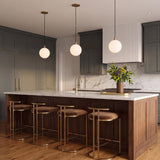 A transitional kitchen features three Soren LED Pendants in brushed brass and opal glass suspended over a walnut island with dark grey cabinets.