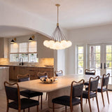 A modern dining room with the Soren 19 Light LED Chandelier in brushed brass and opal glass suspended over a light wood dining table and dark chairs.