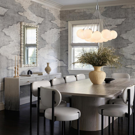 A modern dining room with the Soren 19 Light LED Chandelier 28", Chrome and Opal Glass suspended over a light wood table with gray abstract wallpaper.