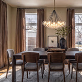 A contemporary dining room with a brushed brass and clear glass globe chandelier suspended over a dark wood table set with walnut and gray upholstered chairs.