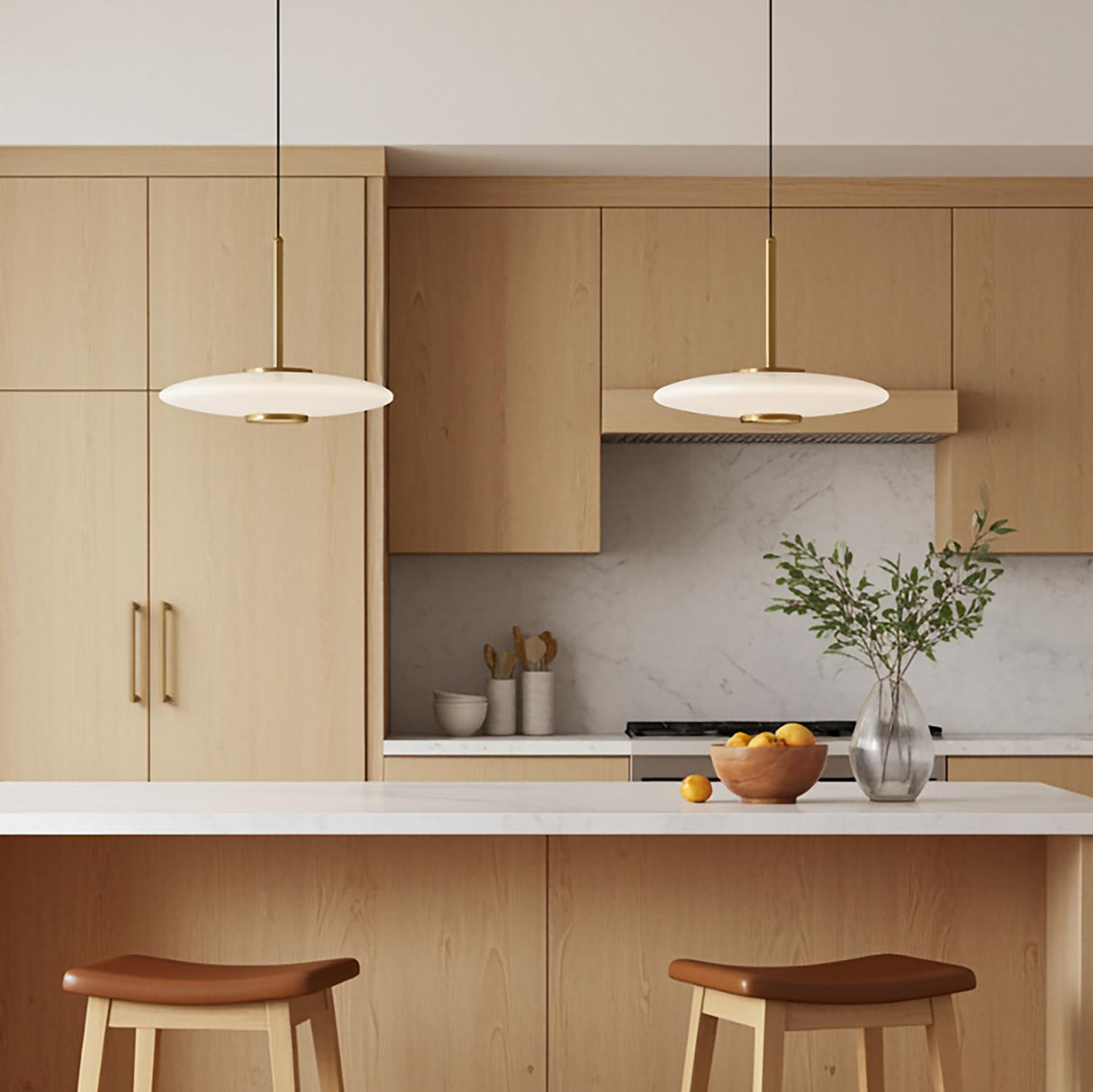 A minimalist kitchen features two Callan LED Pendant 18 inch Aged Brass and Opal Glass fixtures over the island, paired with light wood cabinets and a marble backsplash.