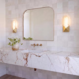 A contemporary bathroom featuring two Lunaire LED Wall Sconces in aged brass and alabaster flanking an arched mirror above a marble vanity and square tile backsplash.