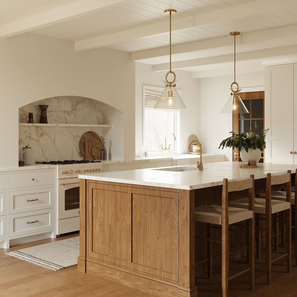 Modern farmhouse kitchen with wooden island, white countertops, and two Aris Medium Pendants, in Aged Brass and Clear Glass.