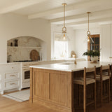 Modern farmhouse kitchen with wooden island, white countertops, and two Aris Medium Pendants, in Aged Brass and Clear Glass.